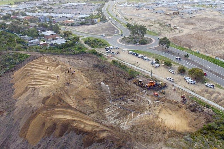Aerial photo of sand dunes with heavy machinery in front of them.