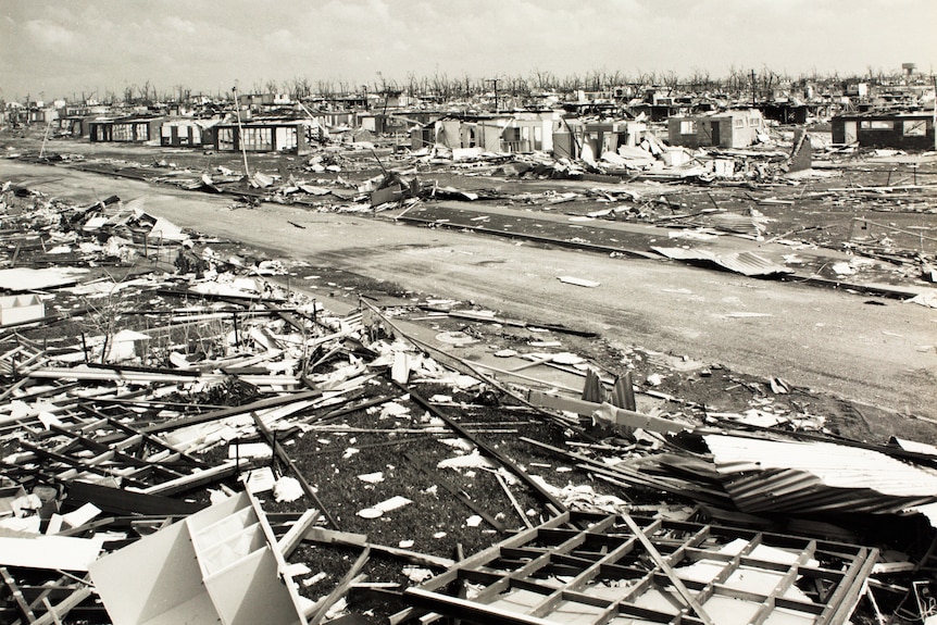 Neighbourhood that looks like it's been blown apart. Houses are completely destroyed, debris is everywher and trees are leafless