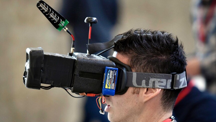 A man wears a large set of virtual reality glasses as he pilots a drone, not in shot.