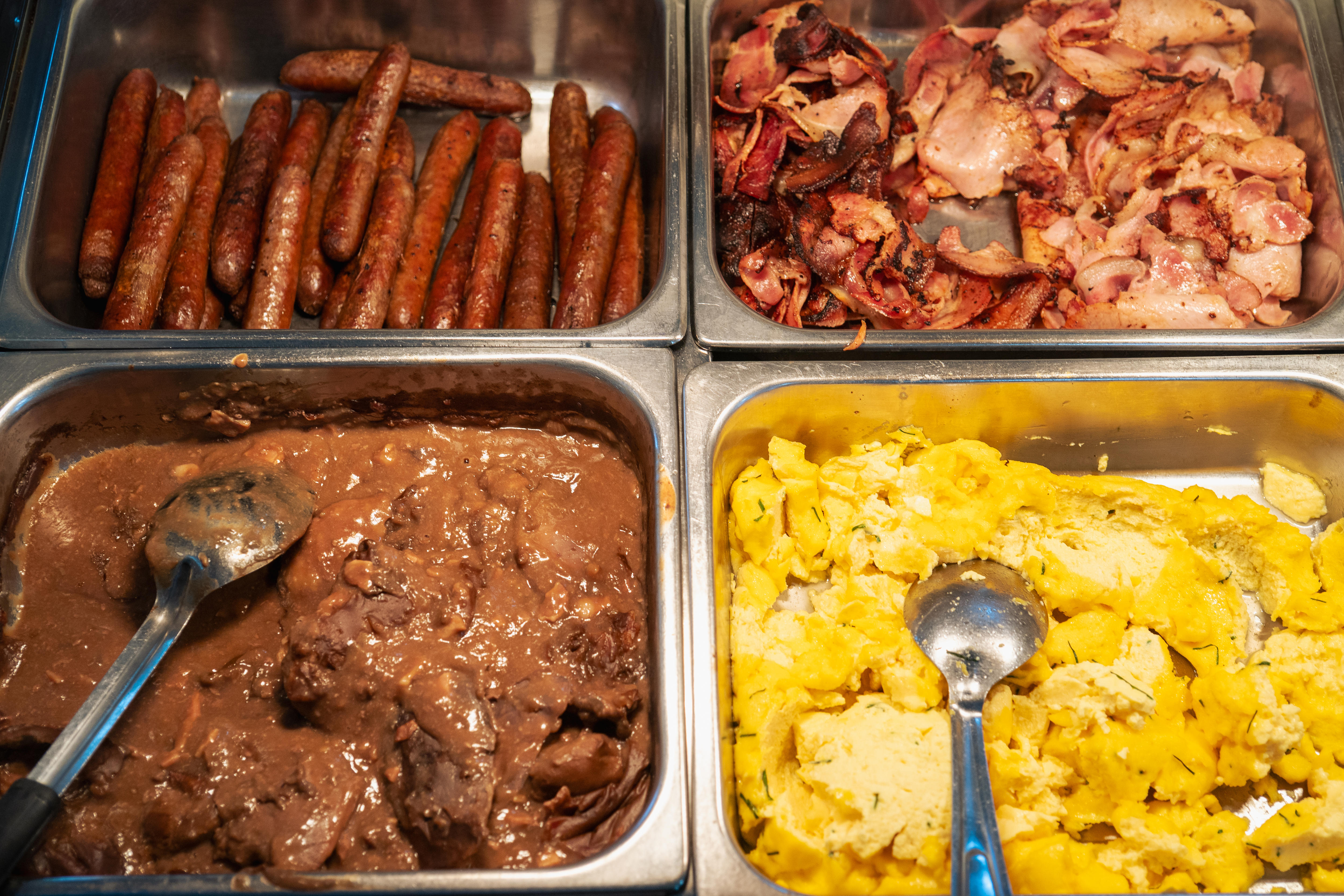 un servidor de buffet calentado con contenedores de cordero asado, huevos revueltos, salchichas y tocino. 
