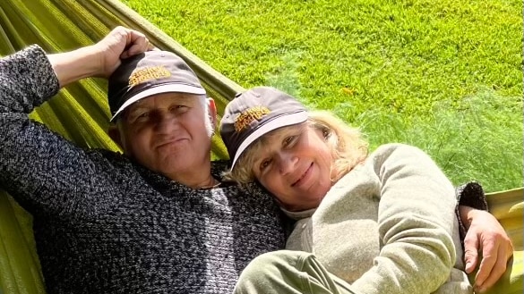 Two people lie in a hammock smiling against green grass