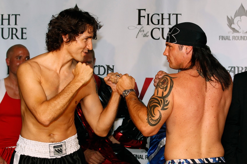 A shirtless Justin Trudeau poses with his fists up next to a shirtless Patrick Brazeau 