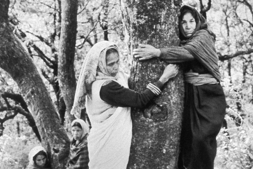Black and white photo of Indian women hugging trees.
