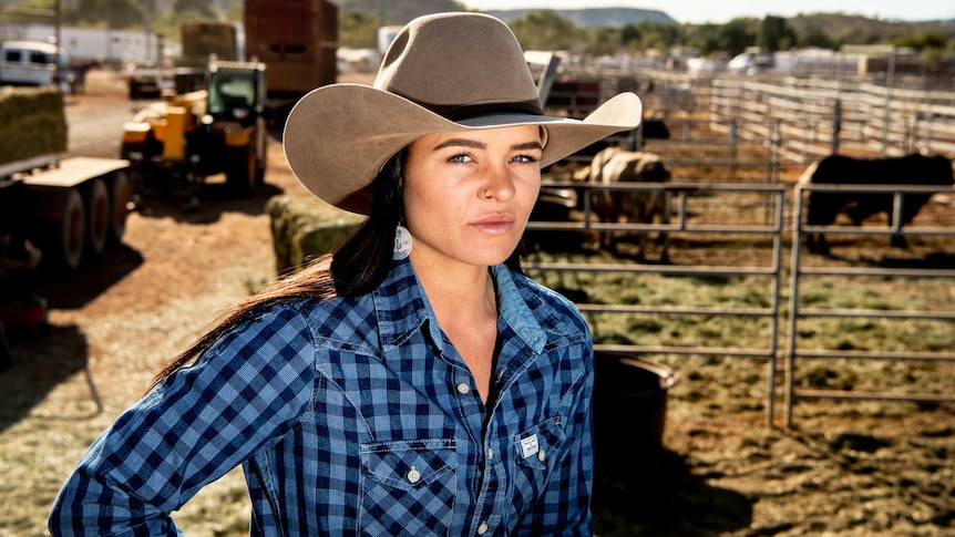 Dakota stands in cattle yards wearing a large hat.