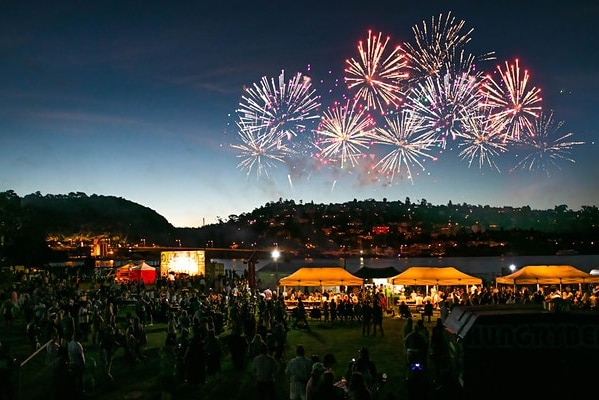 Fireworks in the sky above festival tents beside a river at dusk