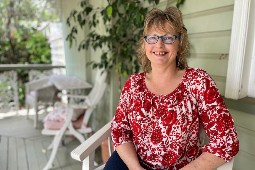 Woman with mid-length blonde hair and a red and white shirt sitting on a verandah. 