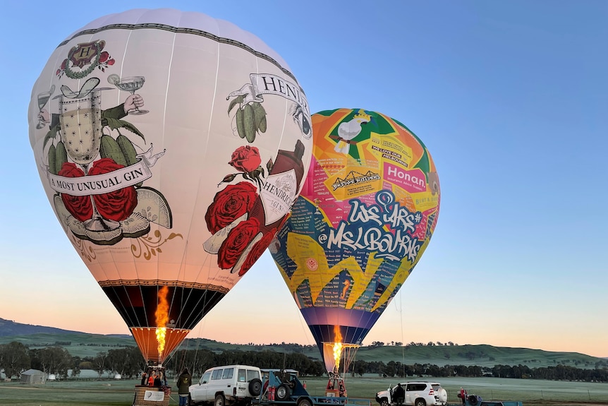 Two hot air balloons sit side by side on the ground