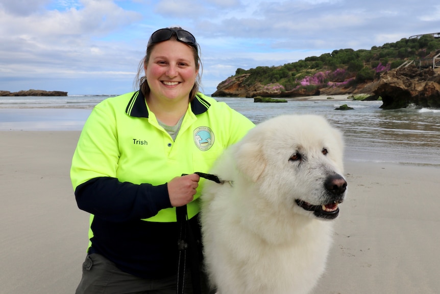 Patricia Corbett sits on the beach with a smiling Tula, Middle Island is in the background