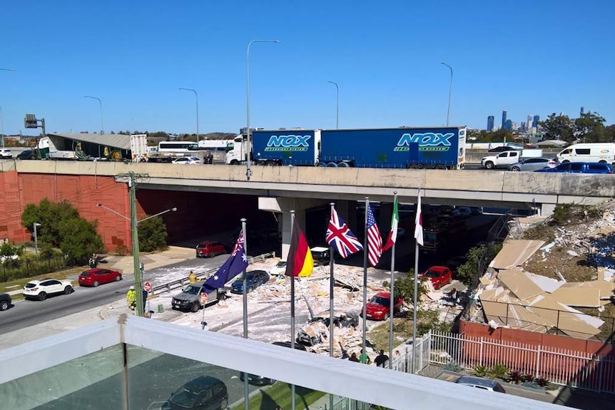 Semi-trailer truck on overpass with lost load of plasterboard on road below.