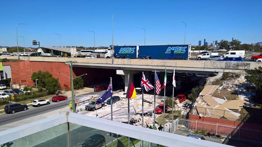 Semi-trailer truck on overpass with lost load of plasterboard on road below.