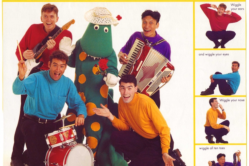 Four men in bright skivvies with musical instruments stand around a person in a dinosaur costume
