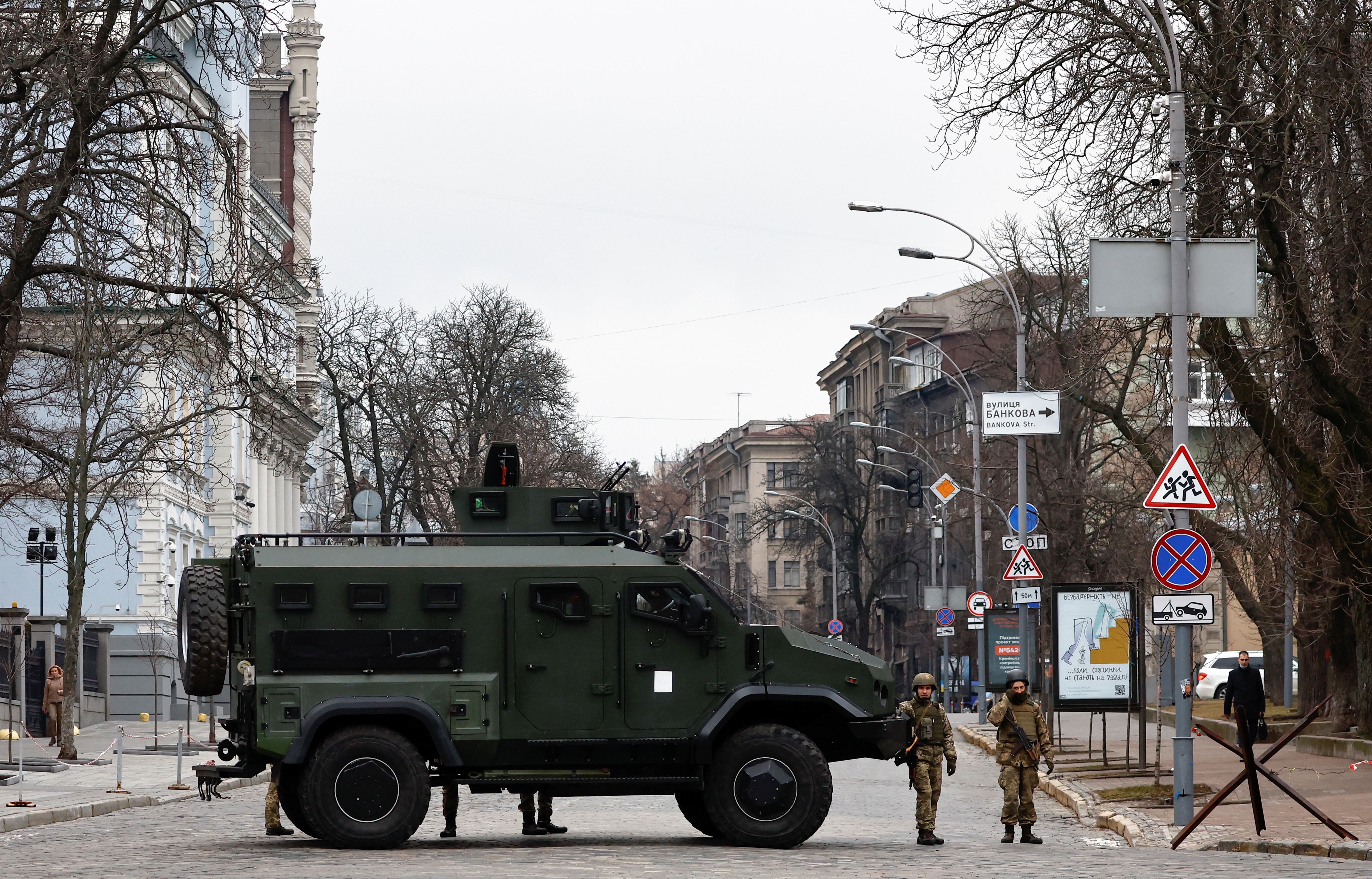 Ukrainian soldiers in camouflage green protective clothing standing next to a dark tank on an empty road