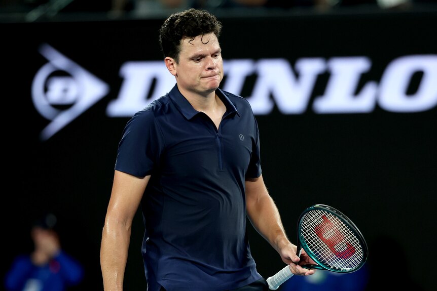 Male tennis player in a dark blue shirt looking dejected because of an injury.