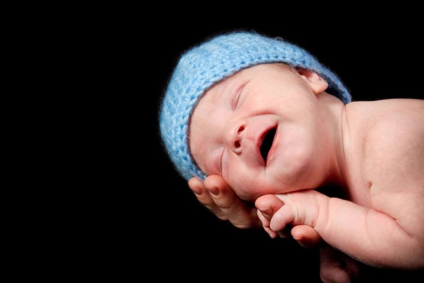 A newborn baby, wearing a blue beanie, lies in his mother's hands