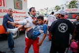 A wounded Palestinian boy is carried by a health worker in front of an ambulance
