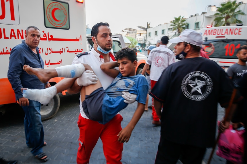 A wounded Palestinian boy is carried by a health worker in front of an ambulance