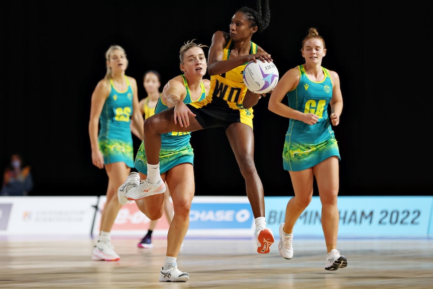 A Jamaican netball player in the air as she holds the ball against Australia.