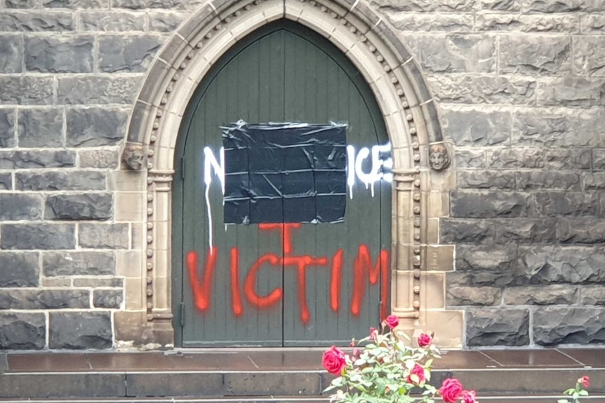 Graffiti on a door at St Patrick's Cathedral, part of which is covered and the word victim in red below.