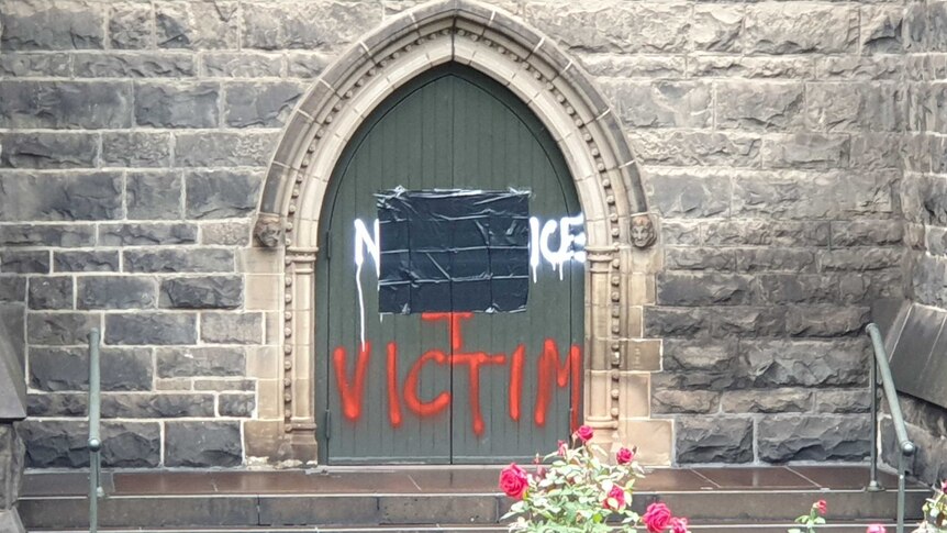 Graffiti on a door at St Patrick's Cathedral, part of which is covered and the word victim in red below.