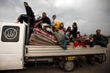 A medium shot of a number of people, including children, sitting and standing amid mattresses in the tray of a truck