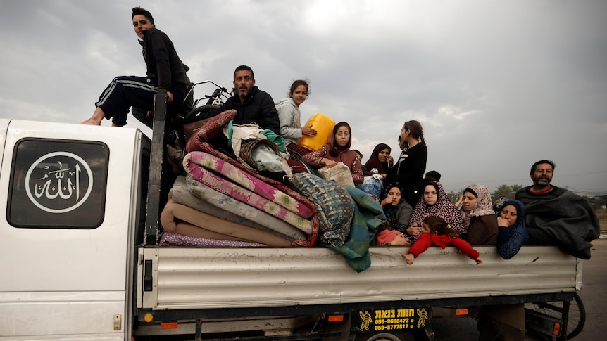 A medium shot of a number of people, including children, sitting and standing amid mattresses in the tray of a truck