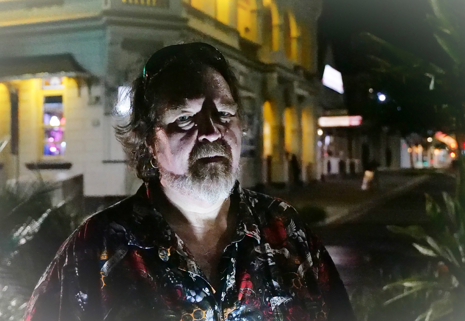 A man standing in shadows in front of a building, with light under his face at night