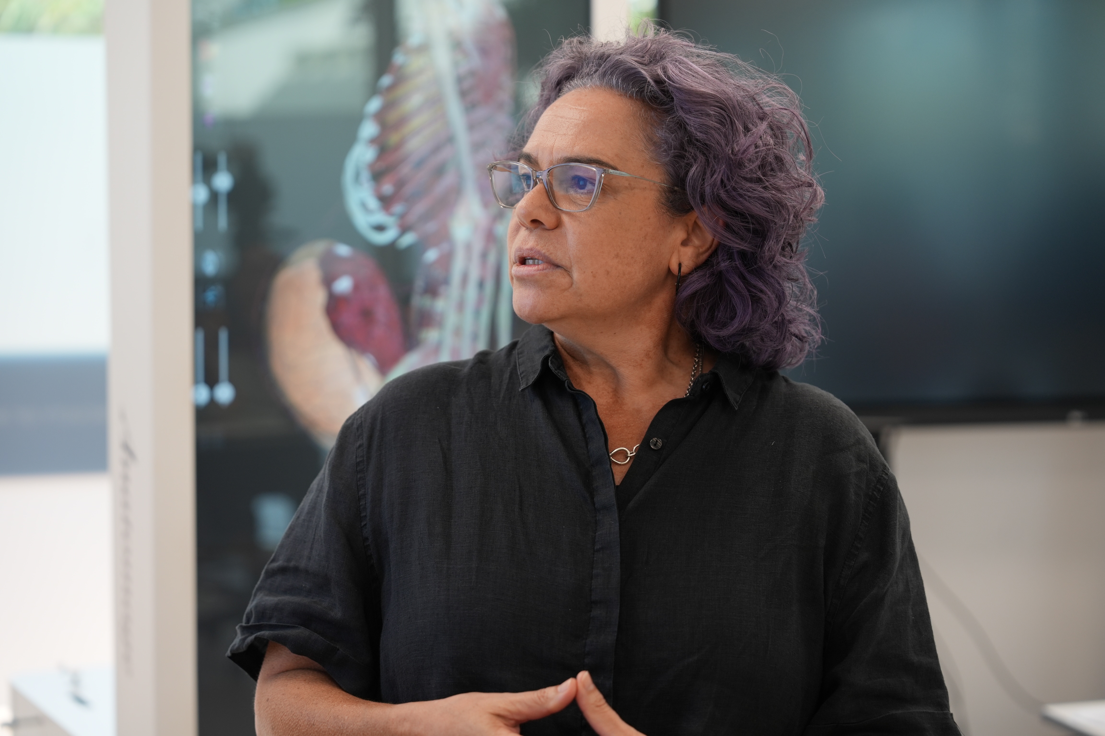 An Indigenous woman with hair dyed purple looks to her side, where information is displayed on-screen for a training session.