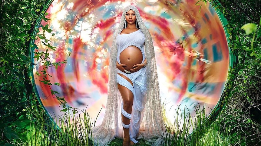 Nicki Minaj holding her pregnant belly, surrounded by foliage, in a Virgin Mary-inspired photo by David LaChapelle.