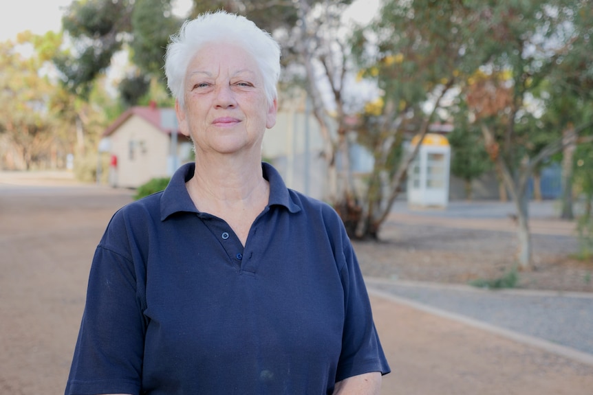 A woman stands in front of cabins with grey hair and a proud expression.