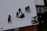 Multiple officers in riot gear making an arrest on a roof as detainees lay down with hands behind their backs.