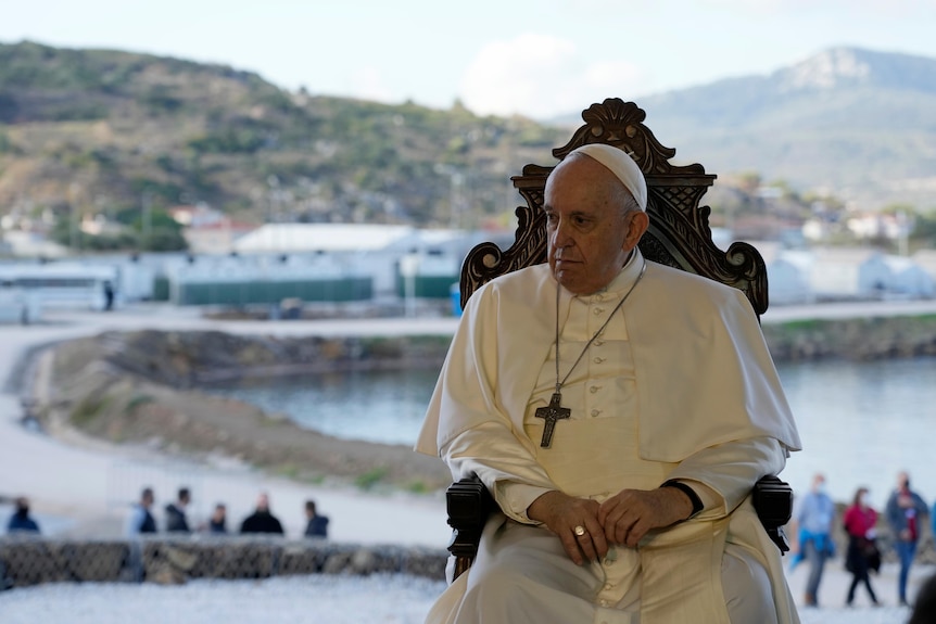 Pope sits on a wooden chair in front of refugee camp