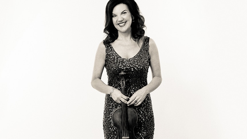A black and white photo of violinist Tasmin Little in a short sequinned cocktail dress holding her violin in front of her.