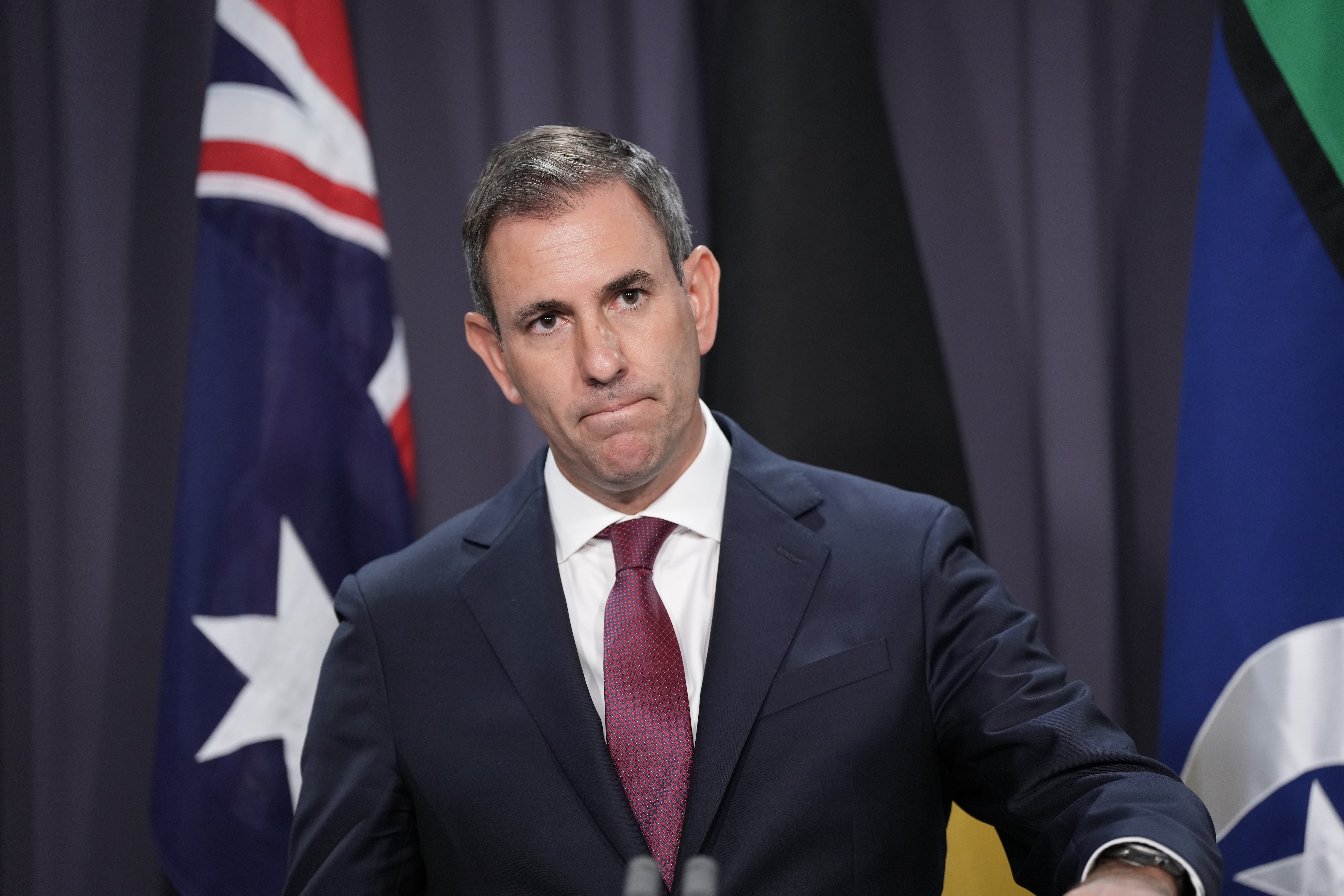 A man wearing a suit in front of an Australian flag. 