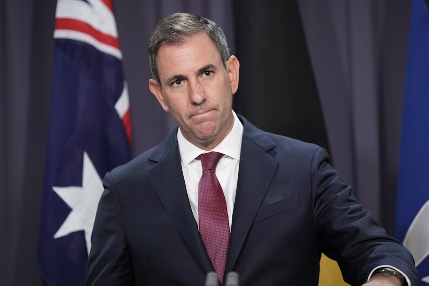 A man wearing a suit in front of an Australian flag. 