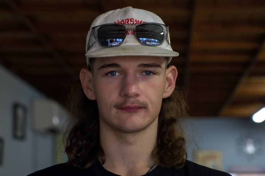 Boy with cap and sunnies and a mullet close up.