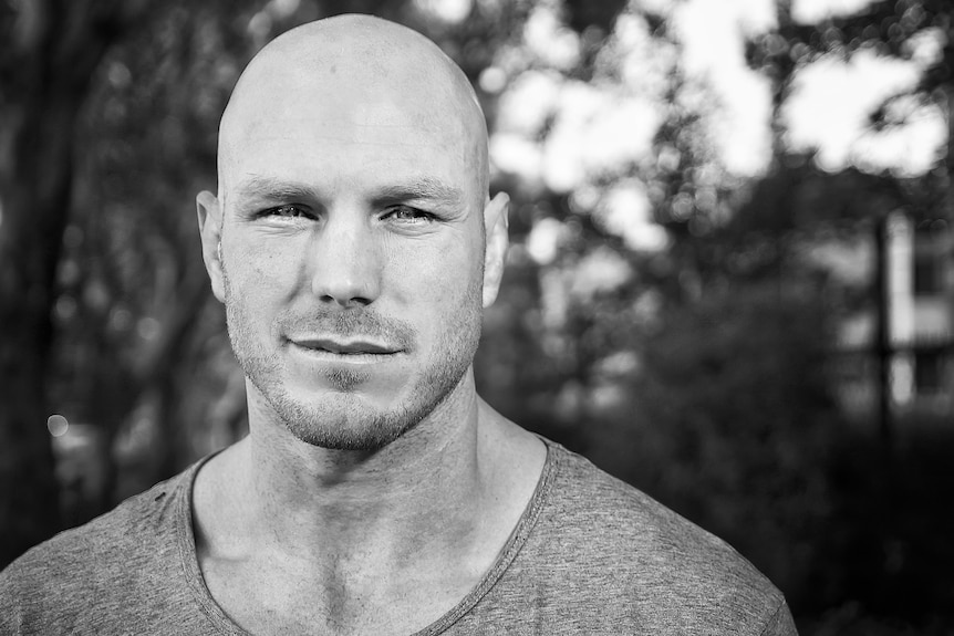 A bald man looks at the camera in a black and white image