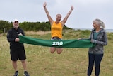 A woman jumps behind a ribbon with the number 250 on it.