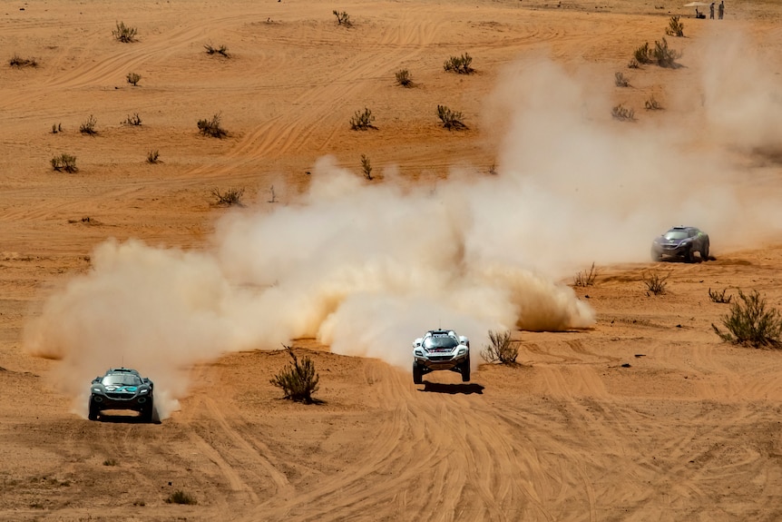 Three cars drive through the desert with dust flying up behind them