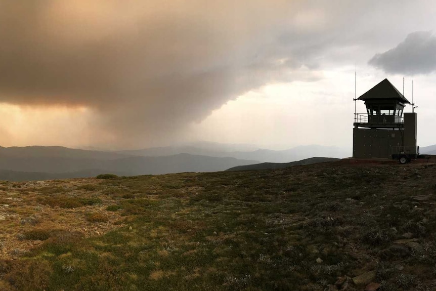 Thick black bushfire smoke clouds hang above a mountainous landscape.