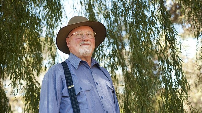 Elderly man stands in front of willow tree