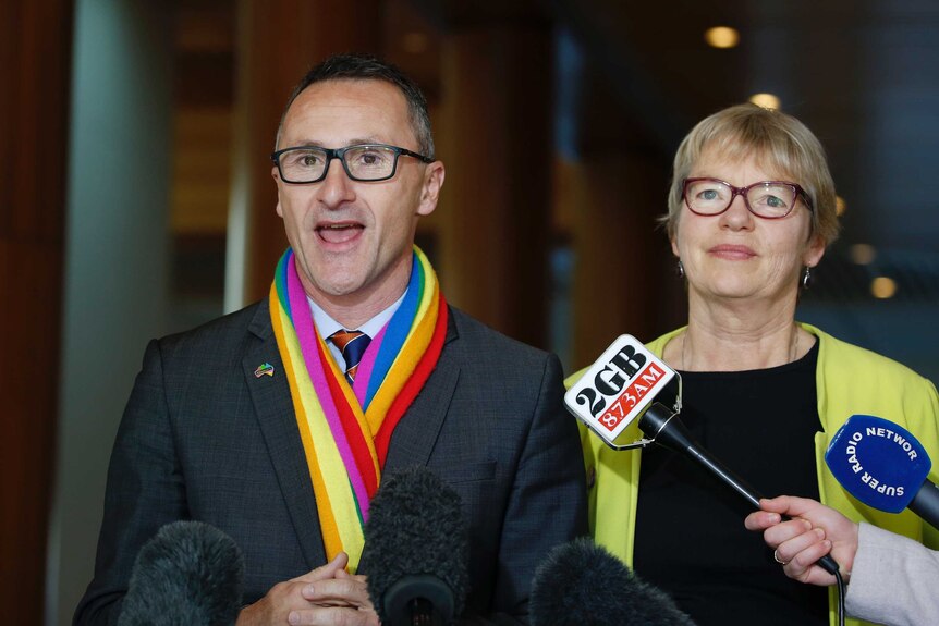 Richard Di Natale, wearing a rainbow-coloured scarf, speaks to reporters. Next to him is Janet Rice.