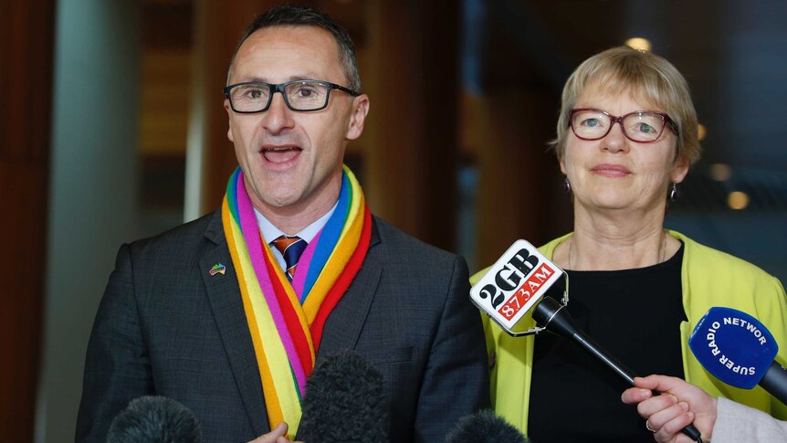 Richard Di Natale, wearing a rainbow-coloured scarf, speaks to reporters. Next to him is Janet Rice.