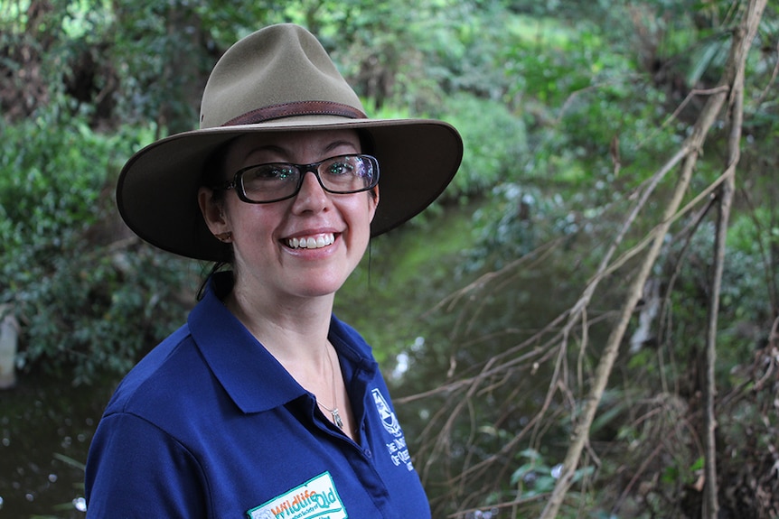 A woman in a blue polo shirt, glasses and an Akubra hat pictured in front of Albany Creek, in north Brisbane.