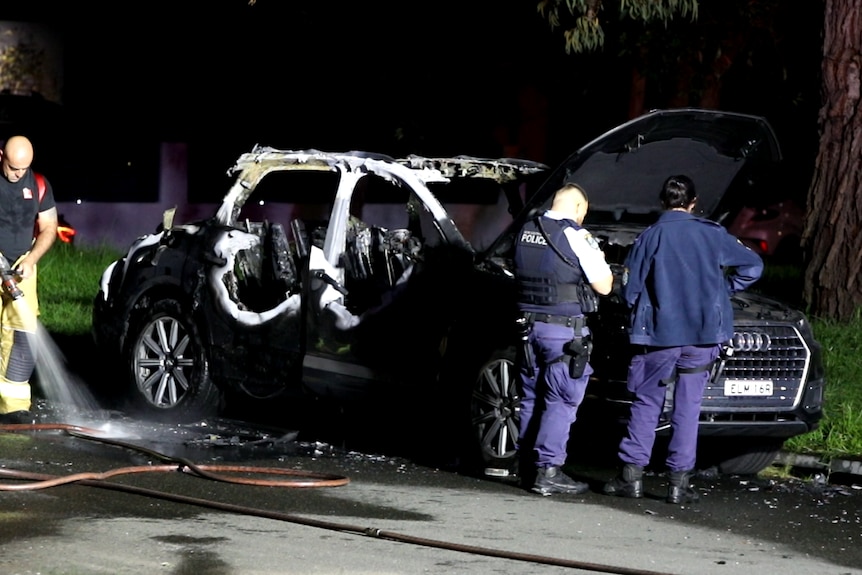 A burnt out car with officers inspecting it 