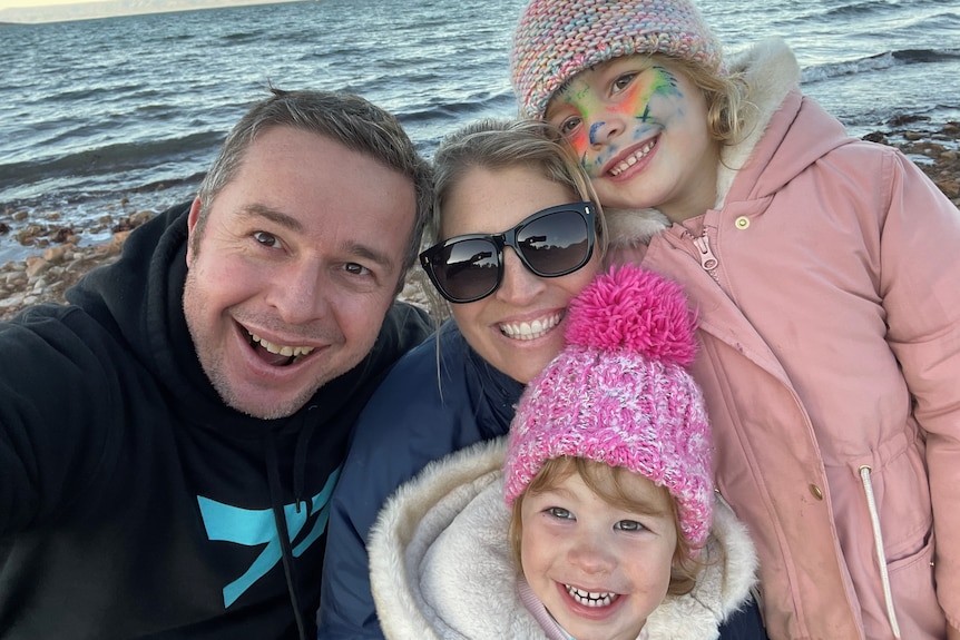 A family of four taking a selfie in front of the ocean.