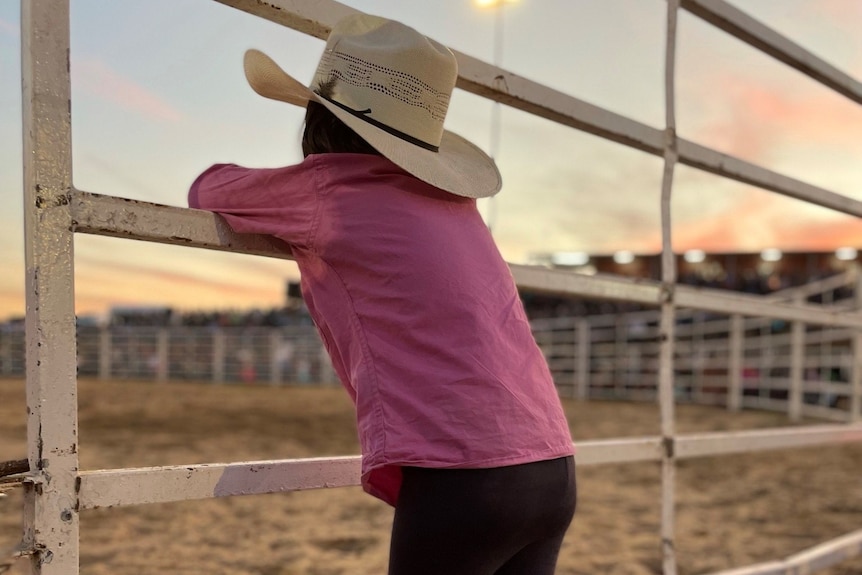 A girl with a cowboy hat leaning on fence