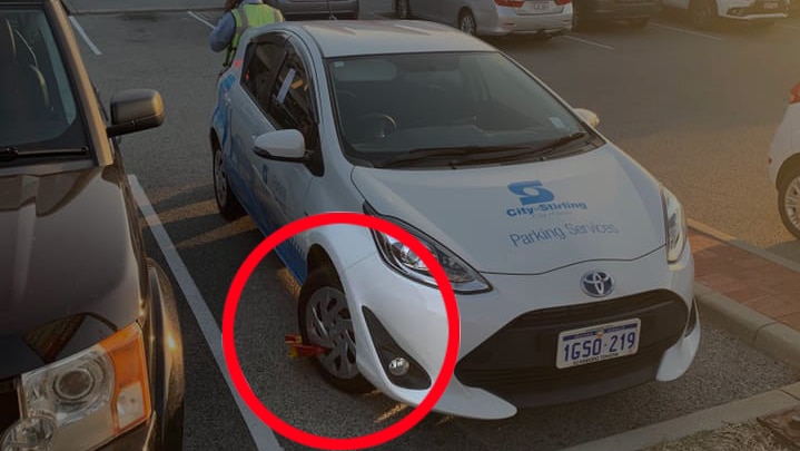 A parking inspector car in a carpark with a wheel clamp on the front wheel.