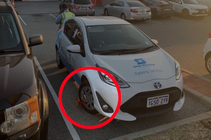 A parking inspector car in a carpark with a wheel clamp on the front wheel.