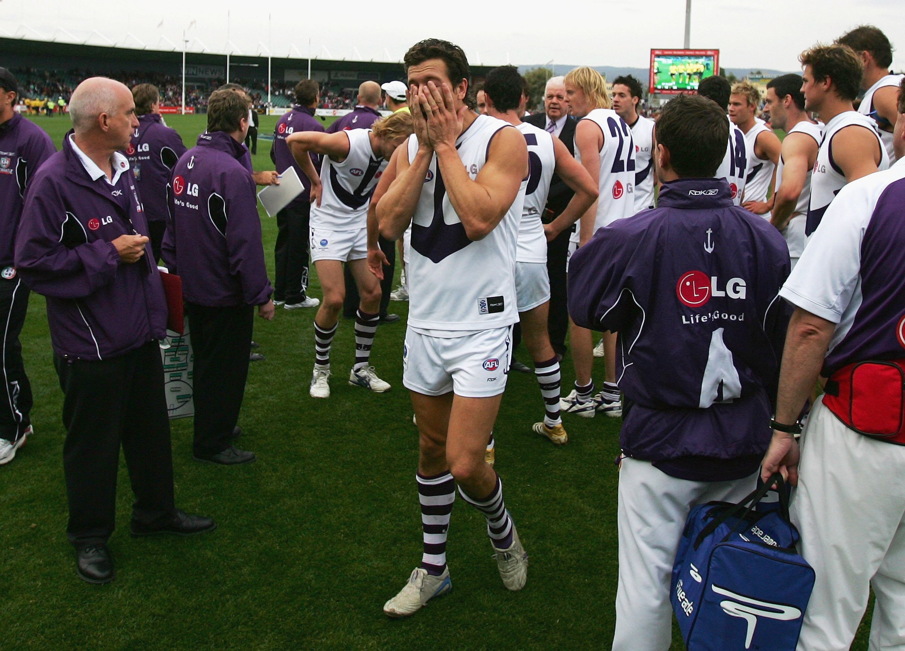 A Fremantle AFL player walks off the ground with his hands over his face, followed by teammates after a game.