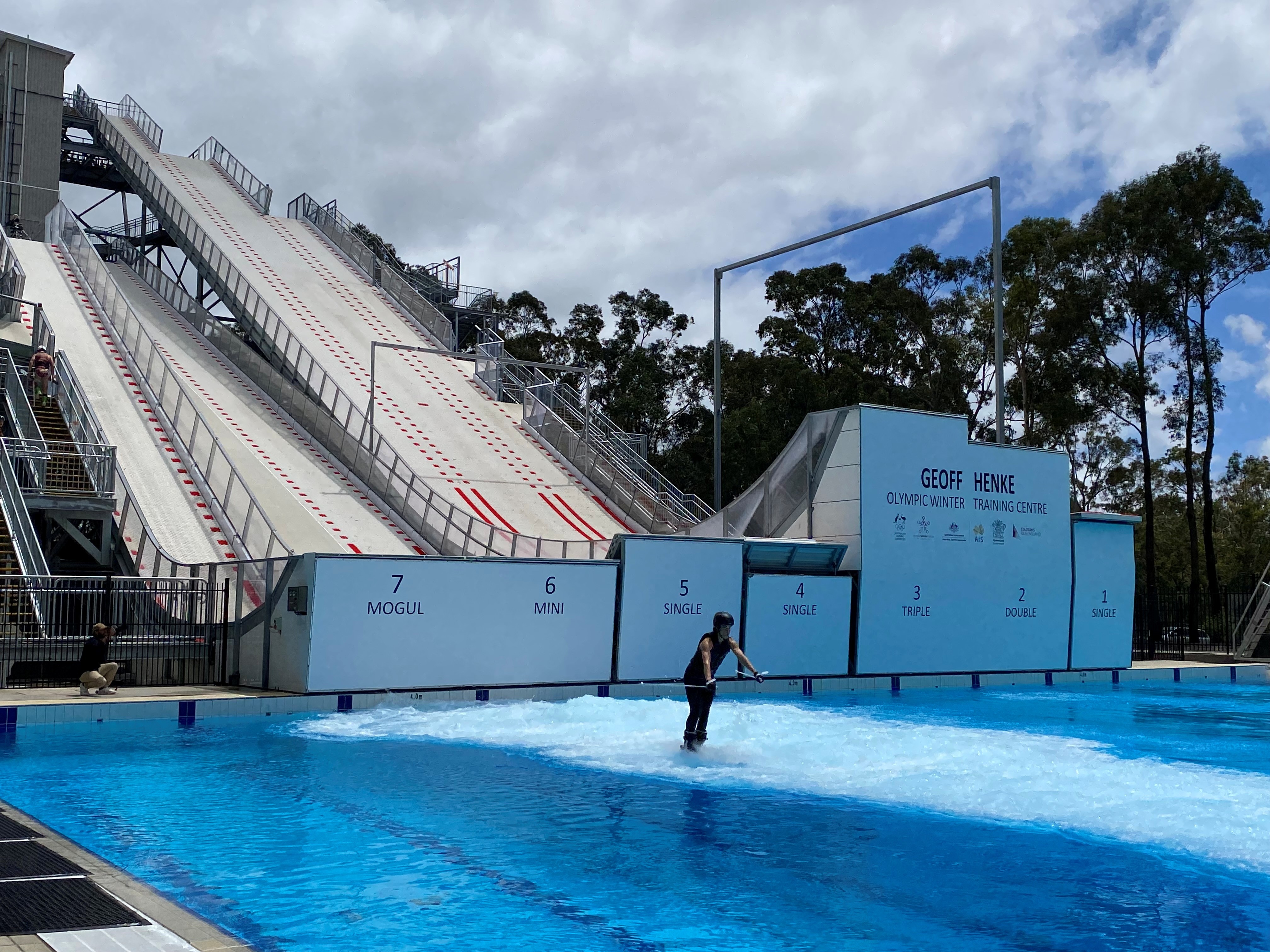 A man skis across an outdoor pool at the bottom of a ramp.